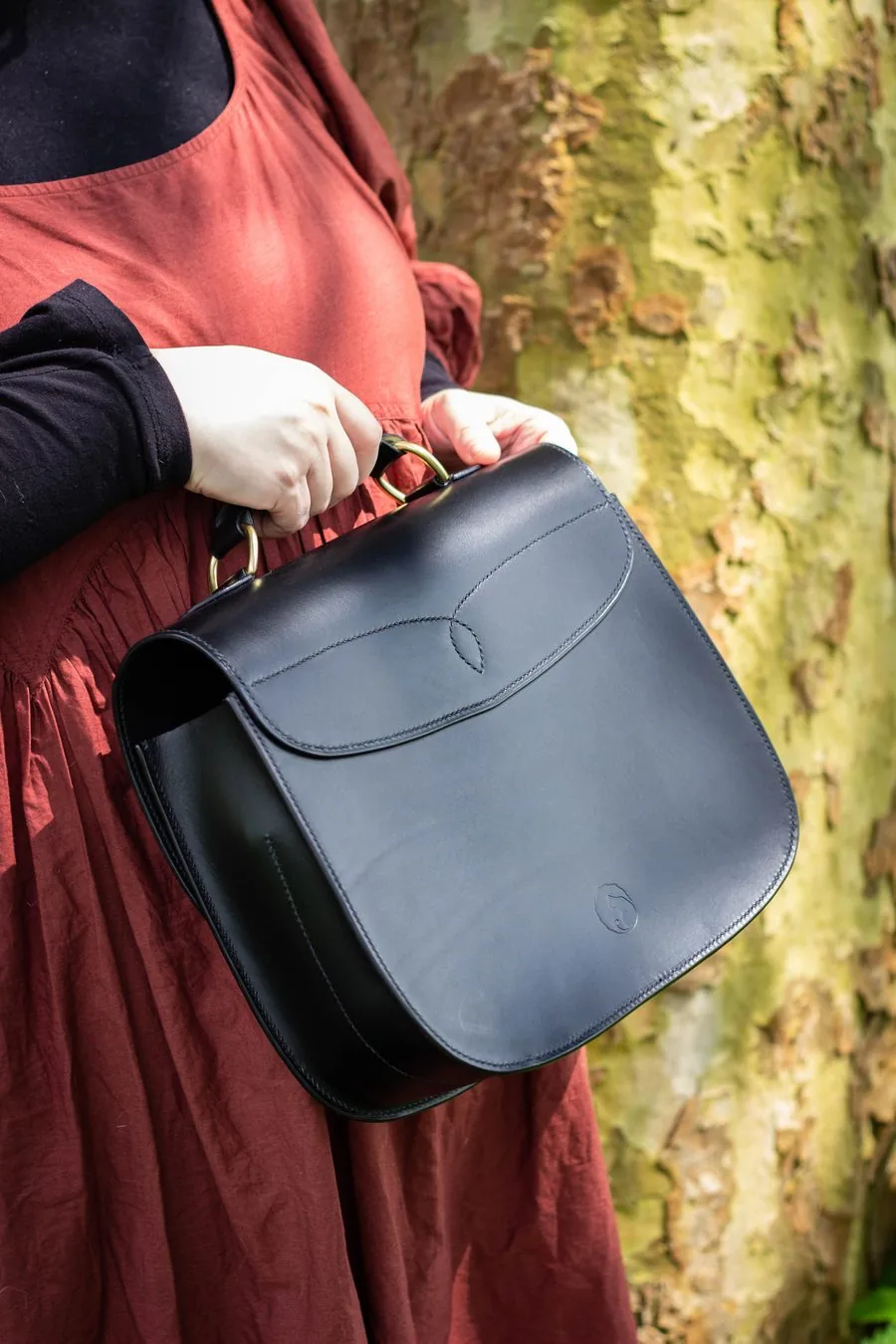 Cartable en cuir noir vu de trois quarts, tenu par sa poignée