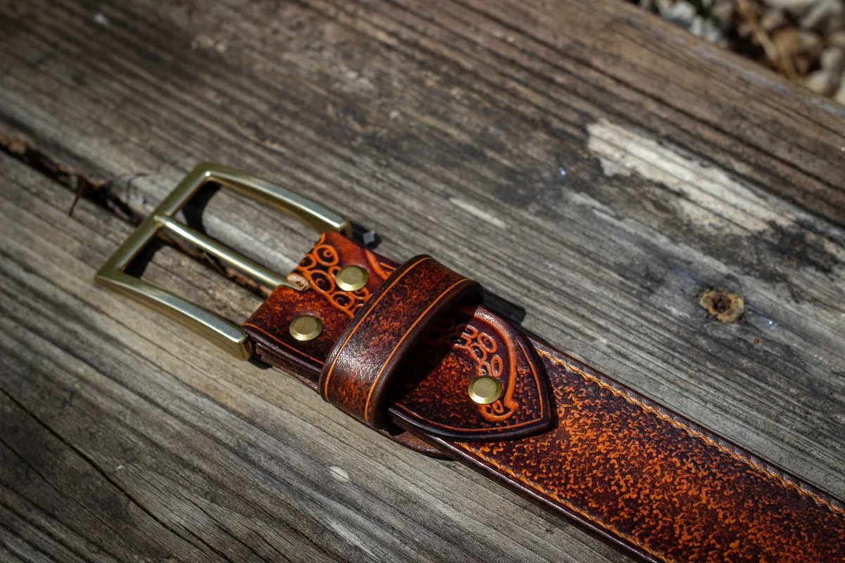 Ceinture en cuir teinté et repoussé, avec sa boucle en laiton, posée sur une planche de bois