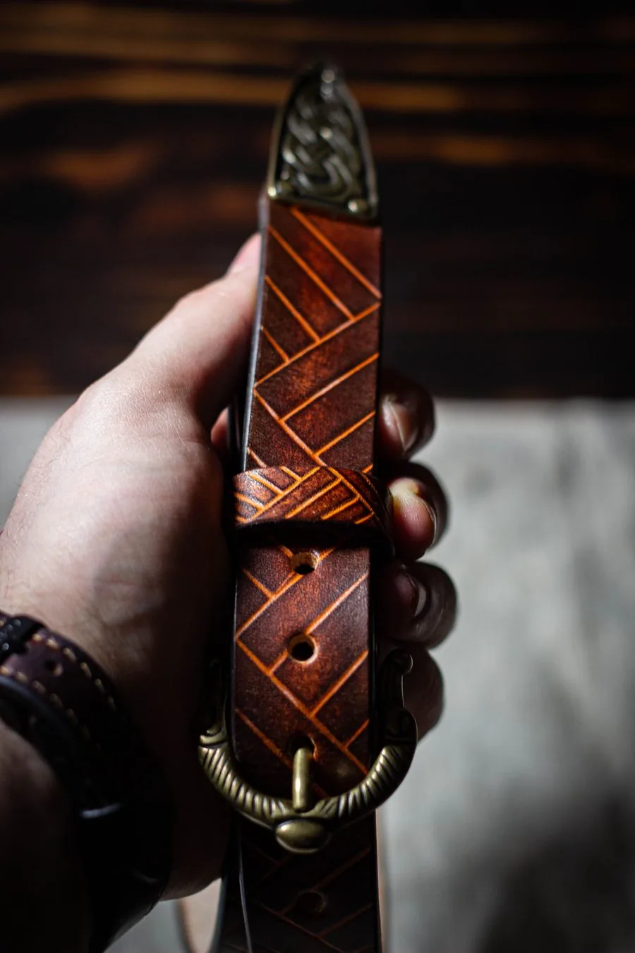 Ceinture gravée de motifs géométriques avec boucle et bout en laiton ouvragés, tenue en main