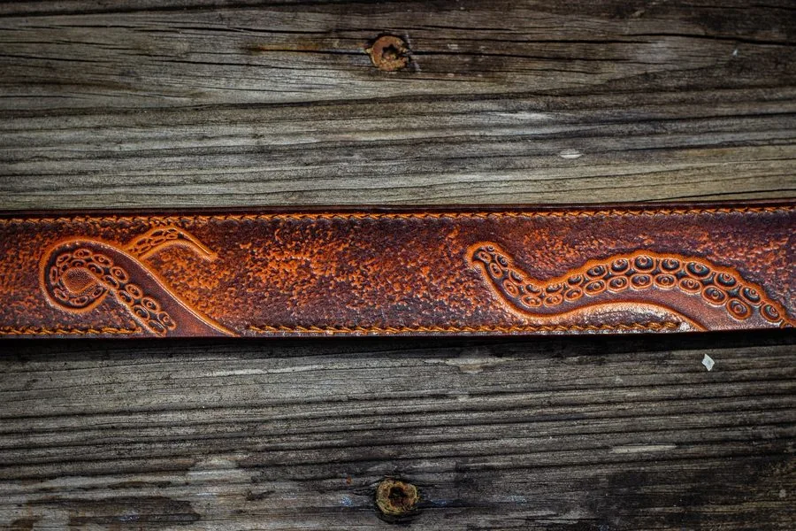 Ceinture repoussée de tentacules sur fond perlé, posée sur du bois