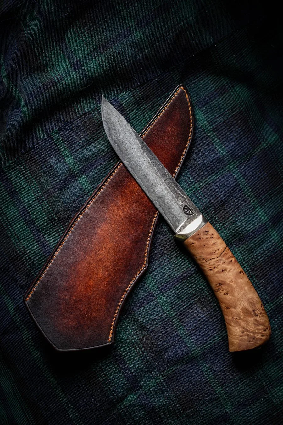 Couteau à manche en bois clair posé sur son étui en cuir teinté, sur un tissu écossais