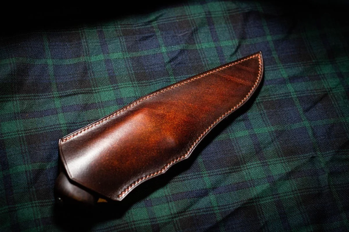 Étui à couteau en cuir teinté à la main et cousu au point sellier, posé sur un tissu tartan