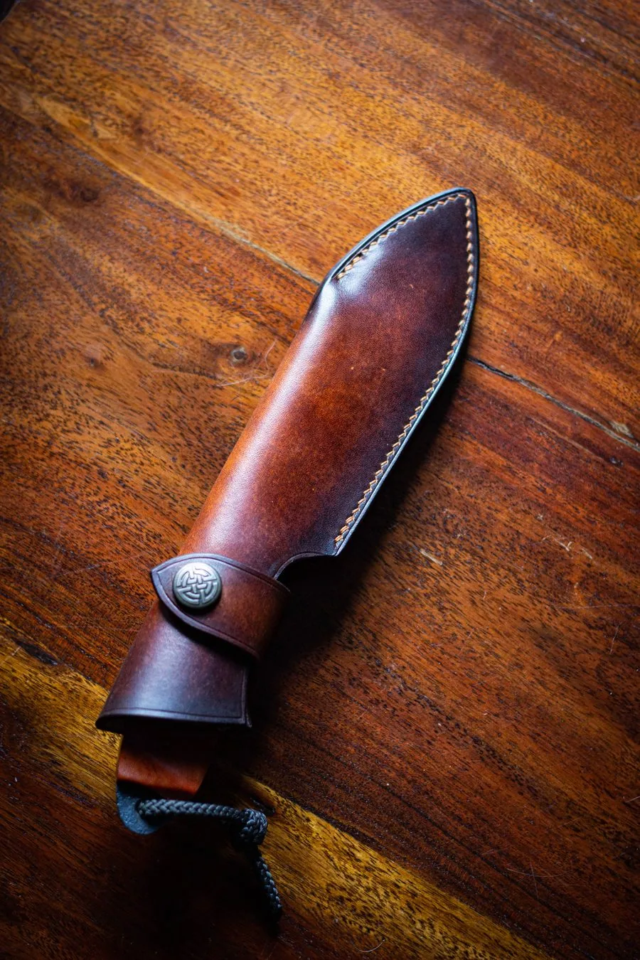 Étui en cuir brun avec sangle de maintien à bouton, sur un plateau en bois