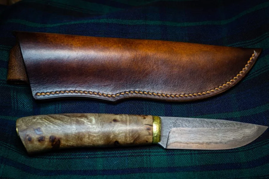 Étui en cuir brun patiné et couteau à manche en bois, sur un tissu écossais