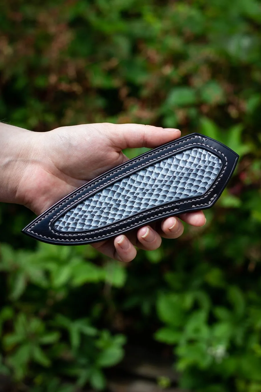 Étui en cuir noir à incrustation au motif écaillé, tenu en main