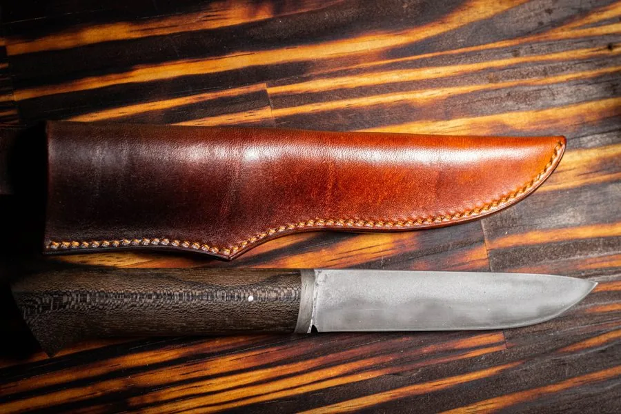 Étui en cuir teinté cognac et son couteau, sur un plateau de bois brûlé
