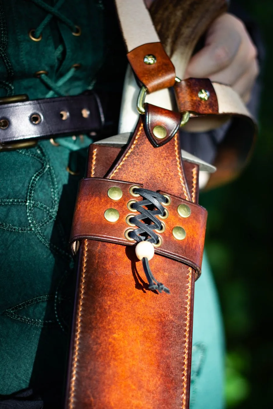 Grand fourreau en cuir fauve avec laçage et rivets en laiton, porté en bandoulière