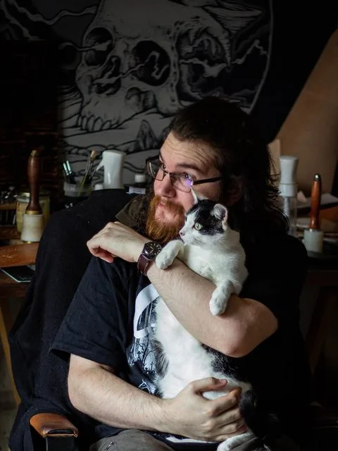 L'artisan de l'atelier du Chat Lunatique à Basse-Indre, avec le chat de l'atelier dans les bras
