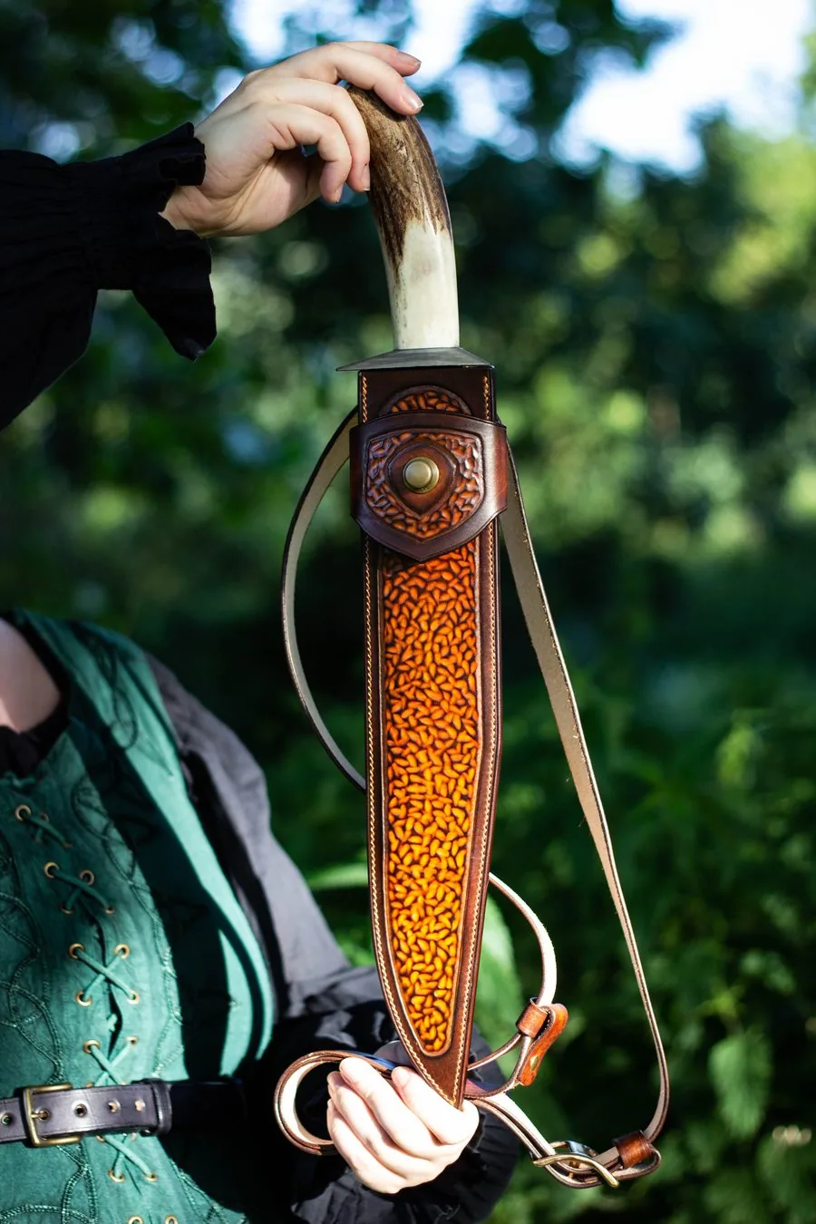 Long fourreau en cuir fauve au fond texturé, avec sa sangle, tenu à bout de bras