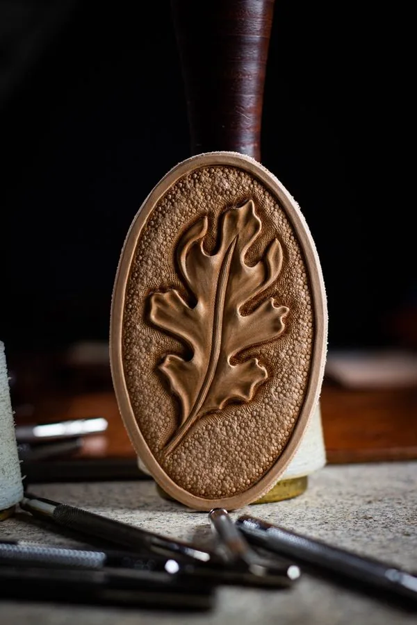 Médaillon en cuir repoussé à la main d'une feuille de chêne, entouré des outils de repoussage