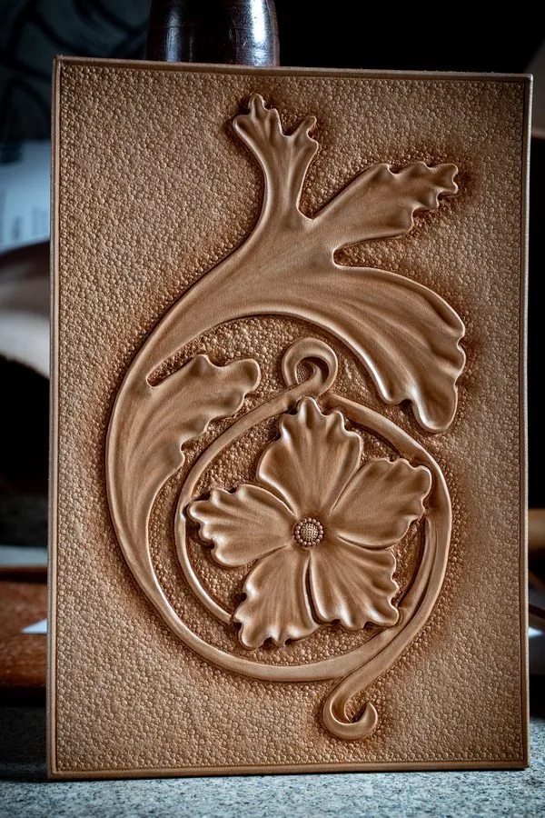 Panneau de cuir naturel repoussé à la main d'une fleur et de rinceaux feuillus sur fond perlé