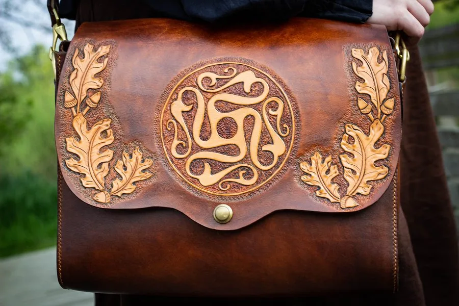 Sac besace en cuir brun, rabat repoussé d'un entrelacs circulaire encadré de feuilles de chêne et de glands