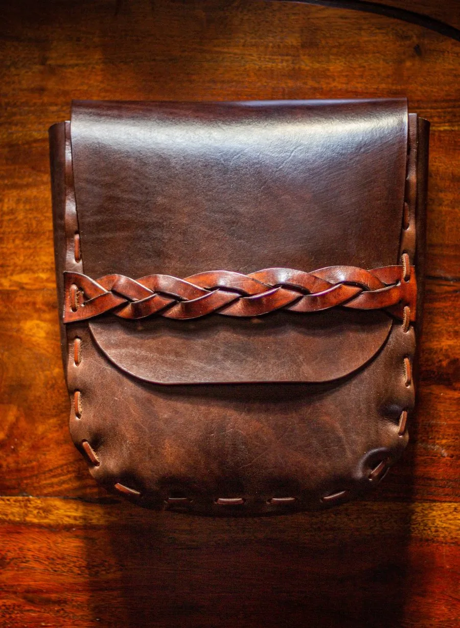 Sac en cuir brun orné d'une tresse de cuir, sur un plateau en bois