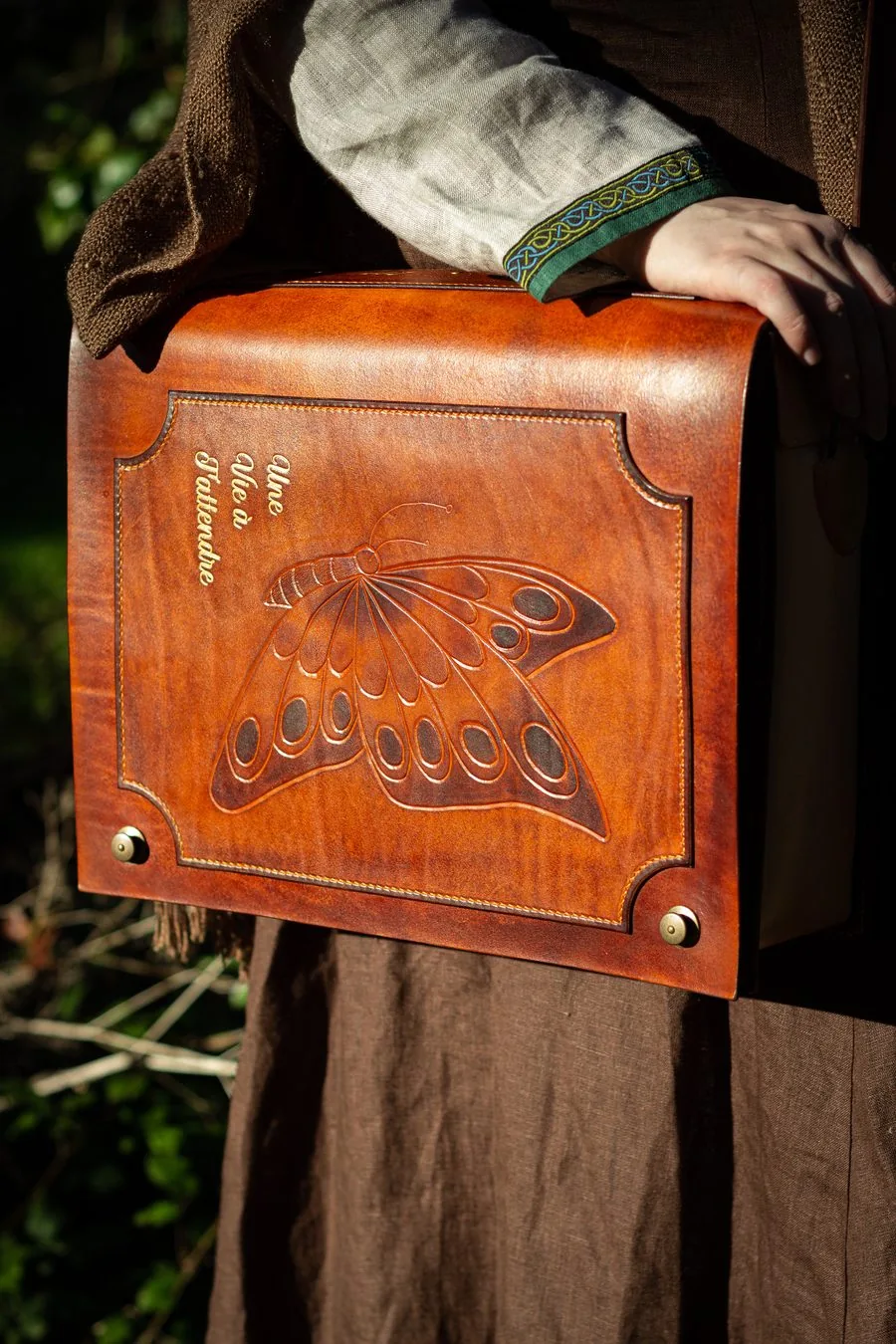 Sac en cuir fauve en forme de livre, repoussé d'un papillon, porté contre la hanche