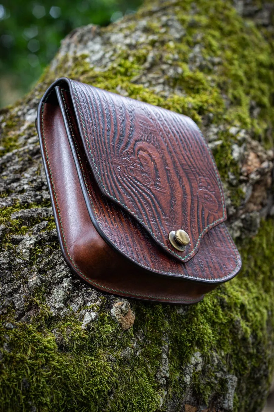 Sacoche repoussée d'un motif de veinage de bois, posée sur un tronc moussu